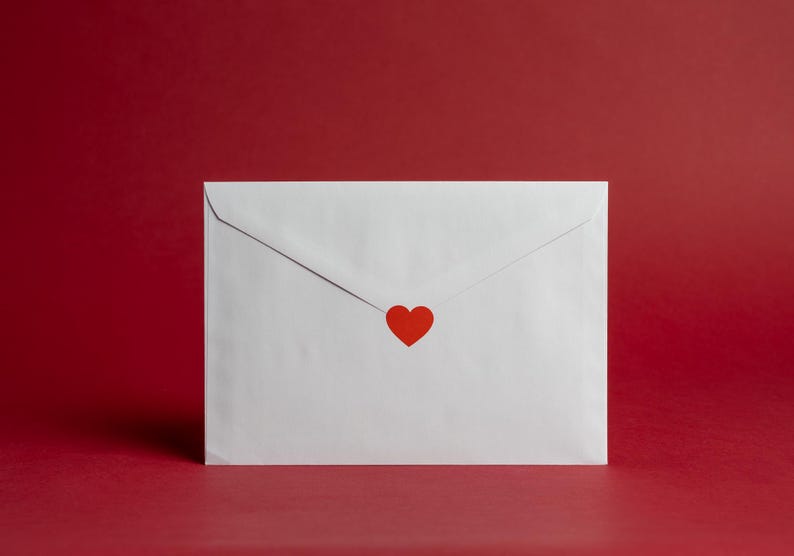May include: A white envelope with a red heart sticker on a red background. The envelope is sealed and centered in the frame. The image has a clean, minimalist aesthetic, perfect for Valentine's Day or other romantic occasions.