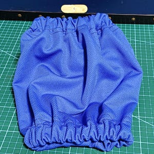 以下が含まれることがあります： グリッド状のテクスチャーが施された鮮やかなブルーの布製アクセサリー。上下の縁にはギャザーを寄せた伸縮性のある開口部があり、中央部分全体に柔らかくプリーツが入ったような外観を作り出しています。