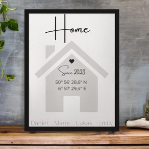 Puede incluir: Impresión enmarcada con la palabra "Home" en escritura cursiva sobre un gráfico de casa. La impresión incluye el texto "Since 2023" y coordenadas. Debajo están los nombres Daniel, Marie, Lukas y Emily. El marco es negro.