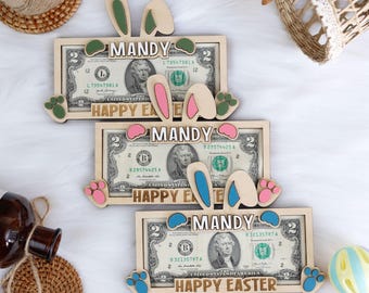 May include: Three wooden money holders with bunny ears and paw prints. Each holder has a $2 bill inside and the name "MANDY" and the text "HAPPY EASTER" printed on it.