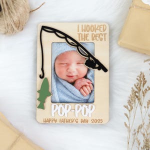 May include: A wooden photo frame with a fishing rod design. The frame has a cutout for a photo and says "I hooked the best Pop-Pop Happy Father's Day 2025".