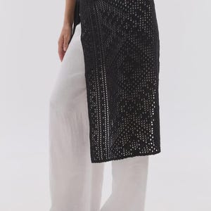 Puede incluir: Una falda negra de tejido abierto superpuesta a unos pantalones blancos. La falda tiene un patrón geométrico y se ata a la cintura. El conjunto es sencillo y elegante, adecuado para el clima cálido. La falda es aproximadamente hasta la rodilla.