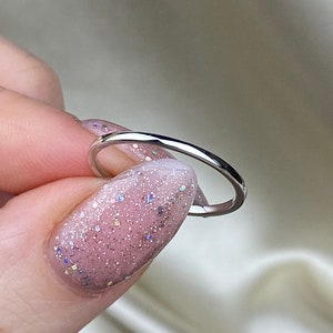 May include: A thin silver band ring. The ring is simple and delicate, with a smooth, polished finish.