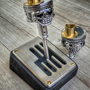 May include: A silver skull-shaped gear shift knob with a gold top, mounted on a black and silver gear shift base with the text "@metalgrimaces".