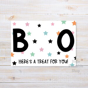 Pode incluir: Uma placa retangular branca com a palavra "BOO" em letras pretas grandes, decorada com estrelas coloridas. O texto "HERE'S A TREAT FOR YOU!" está abaixo.