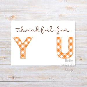 May include: A white card with the words "thankful for YOU" in brown script. The letters "Y" and "U" are in orange and white gingham pattern. The words "Belle Printable Shop" are in a smaller font at the bottom.