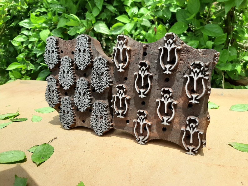 May include: Two wooden printing blocks with intricate floral designs. The block on the left has a repeating pattern of paisley-like motifs, while the block on the right features a repeating pattern of stylized flowers.