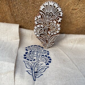 May include: A wooden block printing stamp with a floral design. The stamp is used to create a blue floral print on a white fabric.