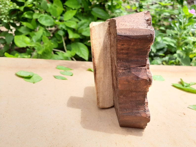 Puede incluir: Primer plano de un bloque de madera con un borde decorativo festoneado. El bloque est&aacute; hecho de madera marr&oacute;n oscura y tiene una tira de madera marr&oacute;n m&aacute;s clara unida a un lado.