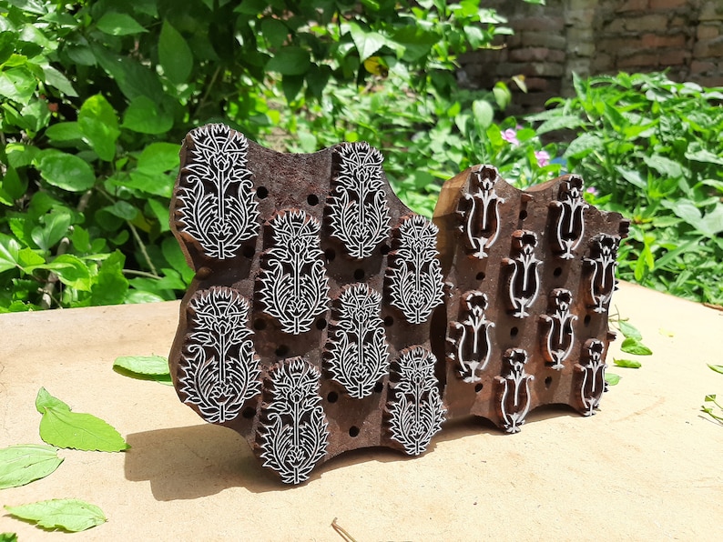May include: Two wooden printing blocks with intricate floral designs. The larger block features a repeating pattern of stylized flowers, while the smaller block has a more geometric design.