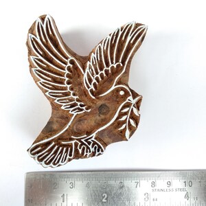 K&ouml;nnte beinhalten: Ein Holzblock-Stempel mit einem wei&szlig;en Design einer Taube, die einen Olivenzweig tr&auml;gt. Der Stempel ist etwa 7,5 cm breit.
