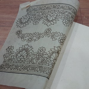 May include: A sheet of white paper with a black floral design printed on it. The design is intricate and includes flowers, leaves, and vines. The paper is folded in half and the design is visible on both sides.
