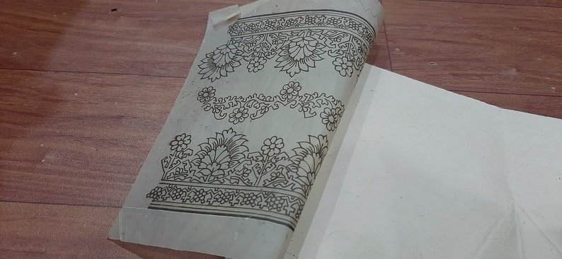 May include: A sheet of white paper with a black floral design printed on it. The design is intricate and includes flowers, leaves, and vines. The paper is folded in half and the design is visible on both sides.