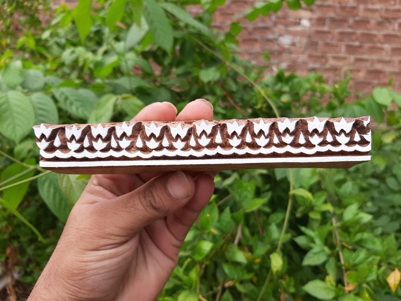 Peut inclure: Un bloc d'impression en bois avec un motif blanc de fleurs stylis&eacute;es r&eacute;p&eacute;t&eacute;es. Le bloc est brun et a une surface lisse.