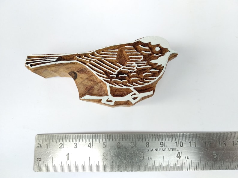 K&ouml;nnte beinhalten: Ein Holzblock-Stempel, der mit einem detaillierten Design eines Vogels geschnitzt ist. Der Vogel ist mit wei&szlig;er Farbe umrandet und hat einen braunen Holzk&ouml;rper.