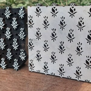 Op de afbeelding: Twee houten drukblokken met een bloemenmotief. De blokken zijn gesneden met een herhalend patroon van gestileerde bloemen. De blokken zijn gemaakt van donker hout en hebben een wit ontwerp.