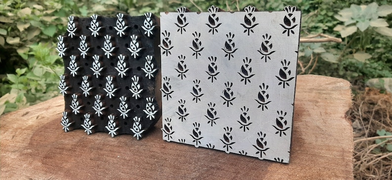 Op de afbeelding: Twee houten drukblokken met een bloemenmotief. De blokken zijn gesneden met een herhalend patroon van gestileerde bloemen. De blokken zijn gemaakt van donker hout en hebben een wit ontwerp.