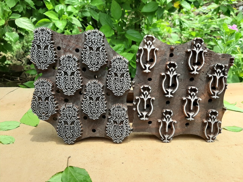 May include: Two wooden printing blocks with intricate floral designs. The block on the left has multiple repeating patterns of a stylized flower with leaves. The block on the right has a repeating pattern of a stylized flower with a curved stem.