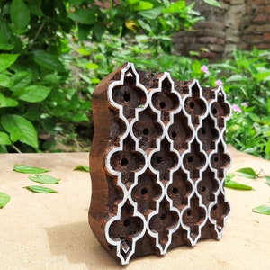 Puede incluir: Un bloque de impresi&oacute;n de madera con un patr&oacute;n geom&eacute;trico tallado en &eacute;l. El bloque es marr&oacute;n y tiene un contorno blanco alrededor del dise&ntilde;o. El bloque est&aacute; sentado sobre una superficie marr&oacute;n claro.