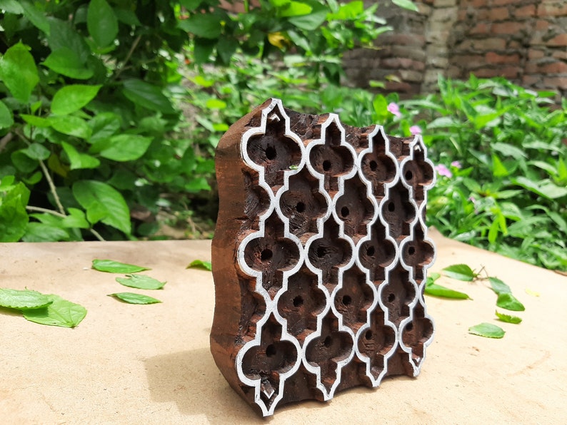 Puede incluir: Un bloque de impresi&oacute;n de madera con un patr&oacute;n geom&eacute;trico tallado en &eacute;l. El bloque es marr&oacute;n y tiene un contorno blanco alrededor del dise&ntilde;o. El bloque est&aacute; sentado sobre una superficie marr&oacute;n claro.