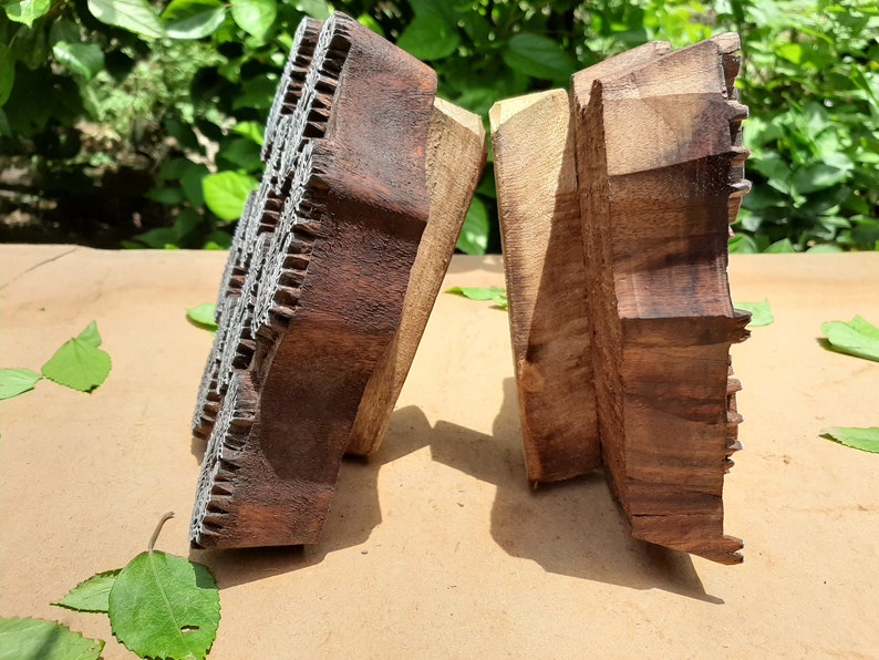 May include: Two wooden printing blocks with intricate carved designs. The blocks are brown and have a worn, rustic appearance. They are likely used for textile printing.