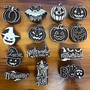 Pode incluir: Uma coleção de catorze blocos de impressão de madeira castanho-escuro com desenhos brancos esculpidos, incluindo abóboras, lanternas, um morcego, um chapéu de bruxa e textos Happy Halloween, Trick or Treat e Halloween.