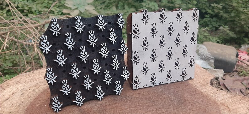 Op de afbeelding: Twee houten drukblokken met bloemmotieven. Het blok links is zwart met witte bloemmotieven. Het blok rechts is wit met zwarte bloemmotieven.