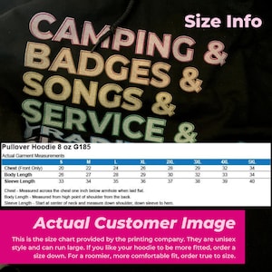 以下が含まれることがあります： レインボーカラーで「Camping & Badges & Songs & Service」と書かれた黒いプルオーバーフーディーのサイズチャート。チャートは、Sから5XLまでのサイズについて、胸囲、着丈、袖丈をインチで表示しています。