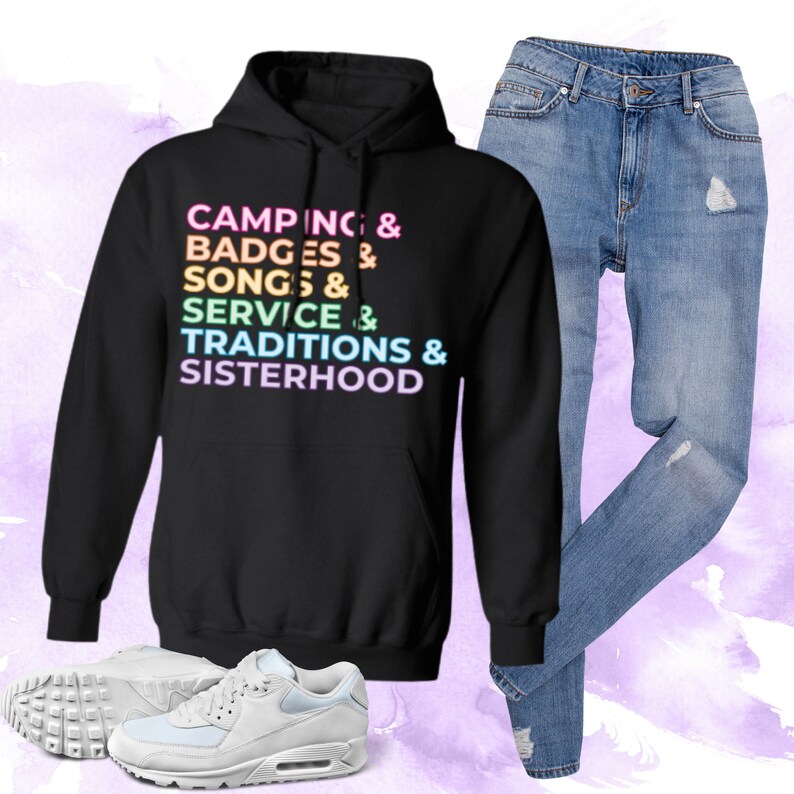 以下が含まれることがあります： レインボーカラーで「Camping & Badges & Songs & Service & Traditions & Sisterhood」と書かれた黒いパーカー。パーカーはライトブルーのジーンズと白いスニーカーと合わせています。