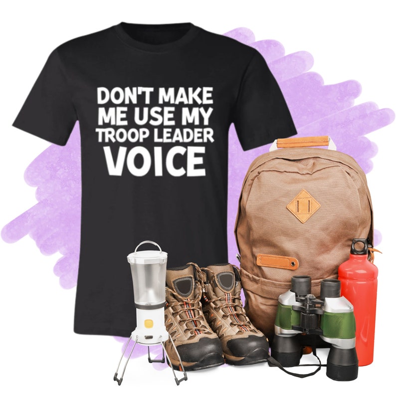 May include: Black t-shirt with white text that reads "Don't make me use my troop leader voice".  The shirt is next to a brown backpack, a pair of brown hiking boots, a lantern, binoculars, and a red water bottle.