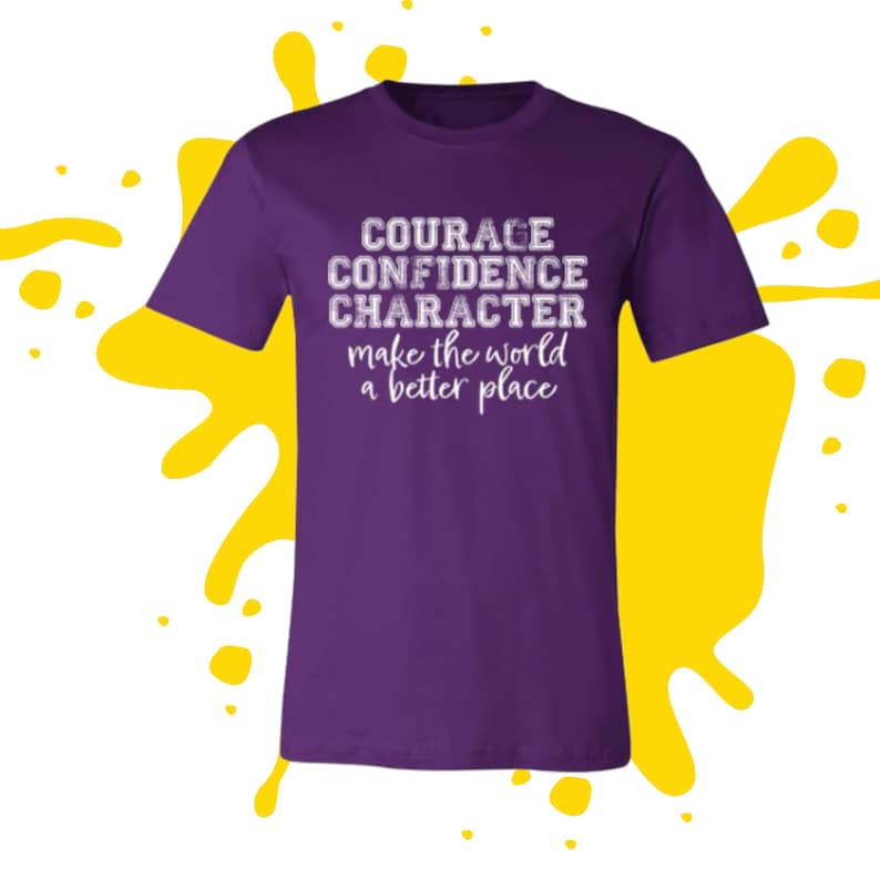 May include: Purple t-shirt with white text that reads "COURAGE CONFIDENCE CHARACTER make the world a better place"