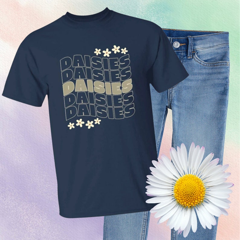 May include: A navy blue t-shirt with a graphic design of the word "DAISIES" repeated five times in a stacked pattern. The word is in a light beige color with a subtle outline. The graphic is surrounded by small white flowers.