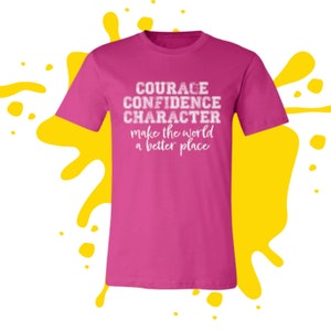 May include: Pink t-shirt with white text that reads "COURAGE CONFIDENCE CHARACTER make the world a better place"