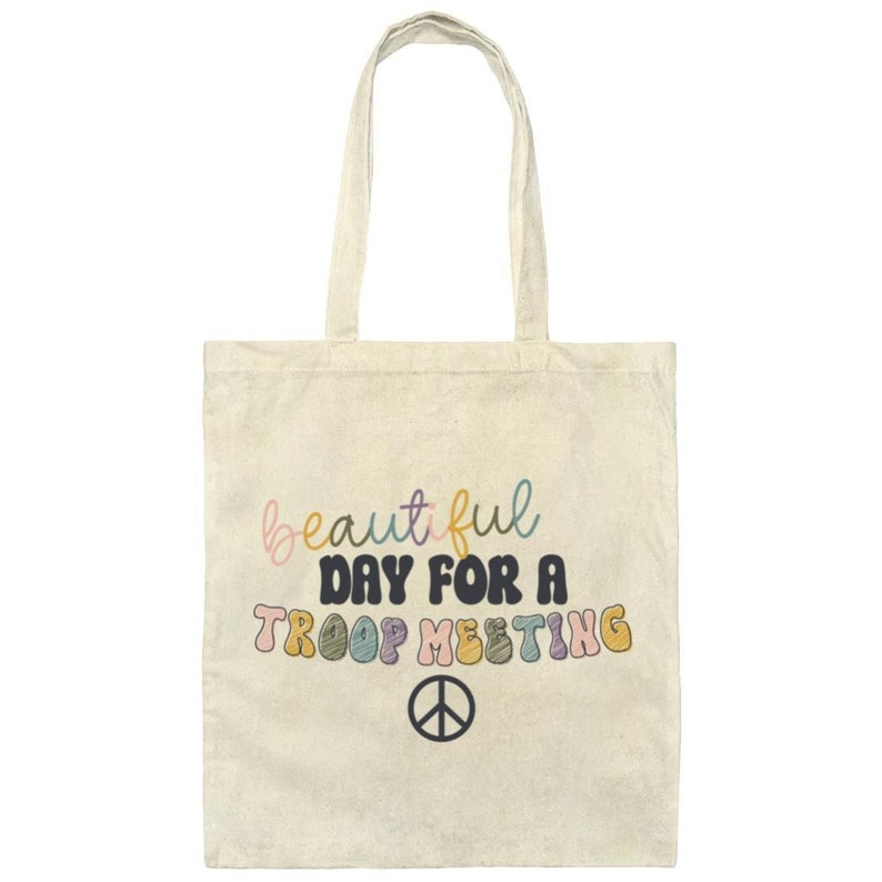 May include: A beige tote bag with the text "beautiful day for a troop meeting" in colorful letters and a peace sign.