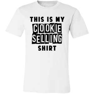 May include: White t-shirt with black text that reads "This is my cookie selling shirt."