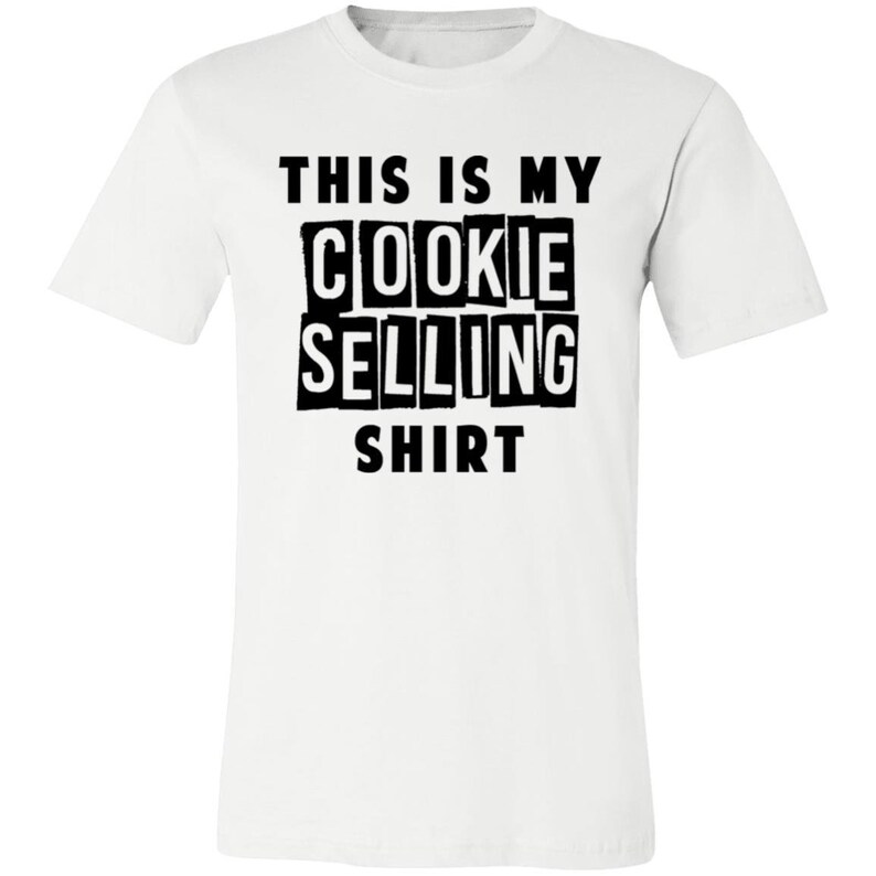May include: White t-shirt with black text that reads "This is my cookie selling shirt."