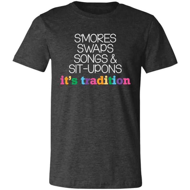 May include: A dark heather grey t-shirt with white text that reads "S'mores Swaps Songs & Sit-Upons it's tradition". The text "it's tradition" is in rainbow colors.