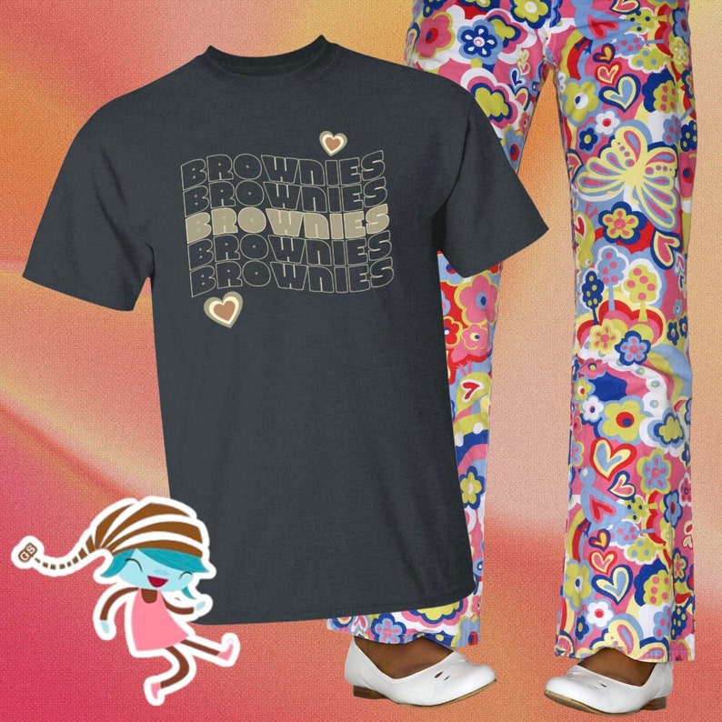 May include: A dark gray t-shirt with the word "BROWNIES" repeated five times in a retro font. The word is stacked vertically and each word is slightly offset from the one above it. A small heart is to the right of the top word and another heart is below the bottom word.