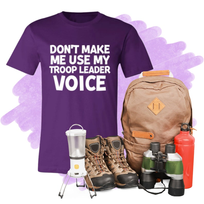 May include: Purple t-shirt with the text "Don't make me use my troop leader voice".  A brown backpack, a pair of brown hiking boots, a green and black pair of binoculars, a red water bottle, and a white camping lantern.