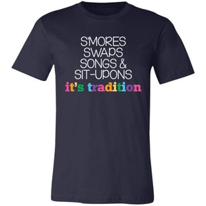 May include: Navy blue t-shirt with white text that reads "S'mores Swaps Songs & Sit-Upons it's tradition". The text is in a rainbow of colors.