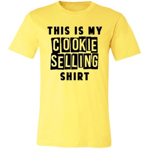 May include: Yellow t-shirt with black text that reads "This is my cookie selling shirt".