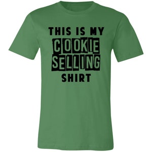 May include: Green t-shirt with black text that reads "This is my cookie selling shirt."
