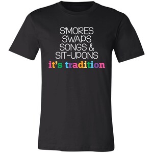 May include: Black t-shirt with white text that reads "S'mores Swaps Songs & Sit-Upons it's tradition". The text "it's tradition" is in rainbow colors.