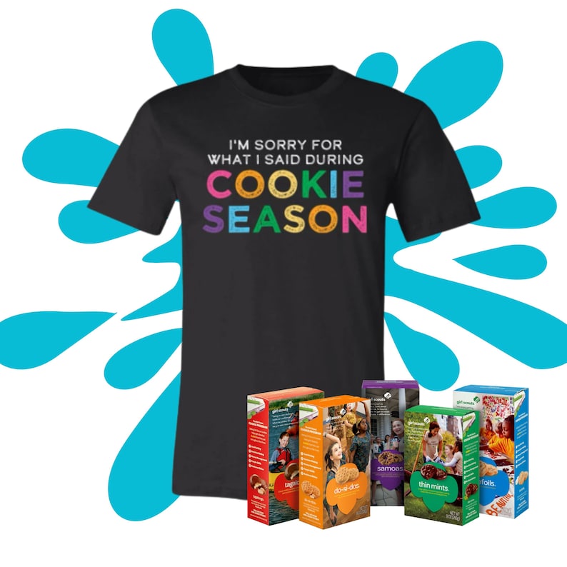 May include: A black t-shirt with the text "I'm sorry for what I said during cookie season" in colorful letters. The shirt is displayed with five boxes of Girl Scout Cookies: Thin Mints, Samoas, Do-si-dos, Tagalongs, and S'mores.
