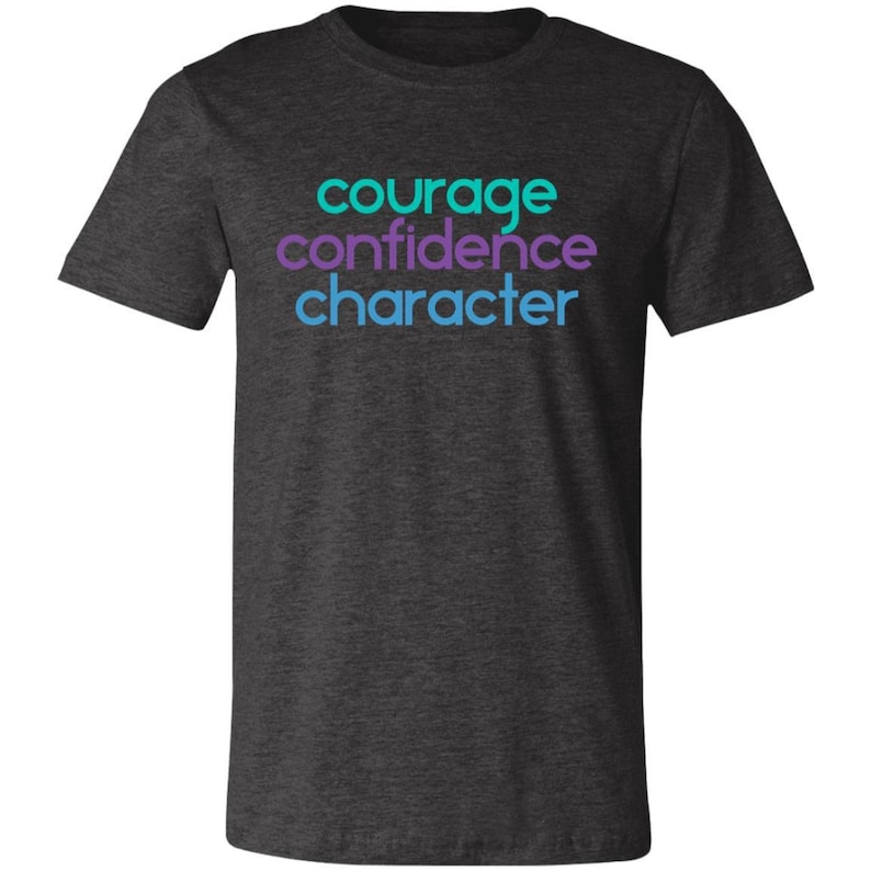 May include: Dark heather grey t-shirt with the words "courage", "confidence", and "character" printed in turquoise and purple.