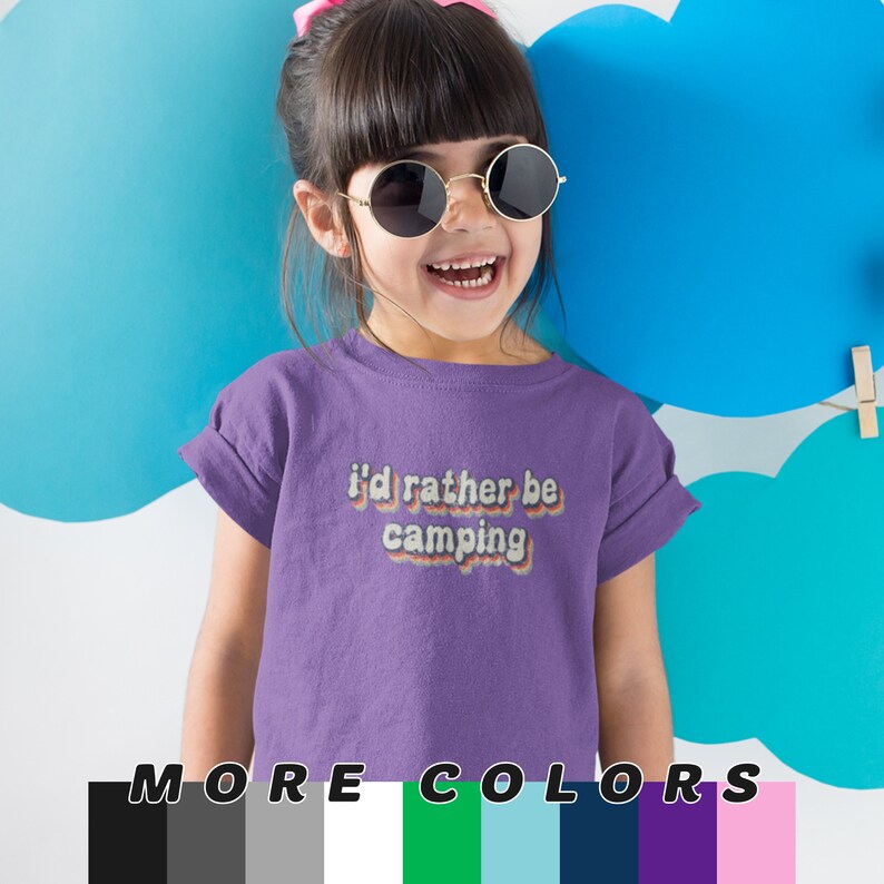 May include: Purple short-sleeved t-shirt with the text "I'd rather be camping" in a retro rainbow font. The shirt is modeled by a young child wearing sunglasses.