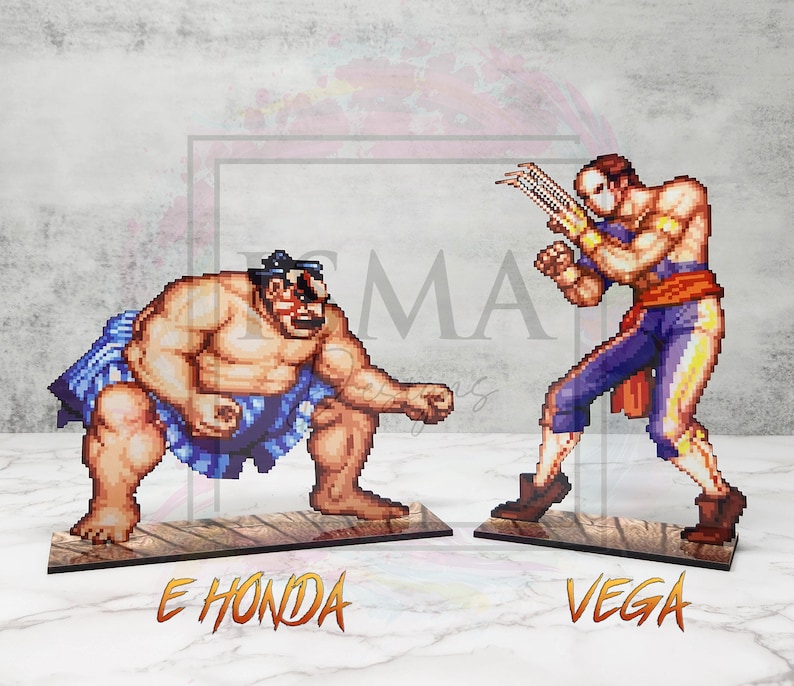 May include: Two pixel art figures from the Street Fighter video game series. E. Honda, a sumo wrestler, is in a fighting stance with his arms raised. Vega, a masked fighter, is in a fighting stance with his claws extended. Both figures are on wooden bases with their names printed below.