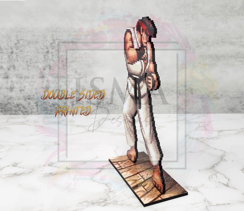 May include: A pixelated figure of a martial arts character in a white gi with a black belt, standing on a wooden platform. The figure is in a fighting stance with one hand raised to their chin. The figure is double-sided printed.