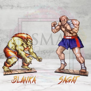 May include: Two pixel art figures from the Street Fighter video game series. Blanka, a green, humanoid creature with red shorts, is on the left. Sagat, a muscular man with a red headband and blue shorts, is on the right. Both figures are standing on wooden bases with their names printed below.