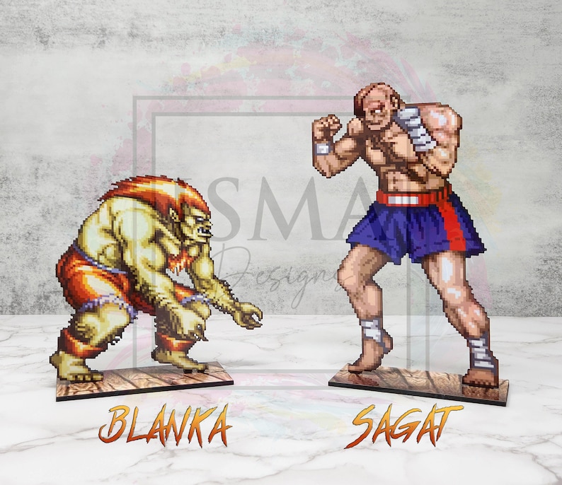 May include: Two pixel art figures from the Street Fighter video game series. Blanka, a green, humanoid creature with red shorts, is on the left. Sagat, a muscular man with a red headband and blue shorts, is on the right. Both figures are standing on wooden bases with their names printed below.